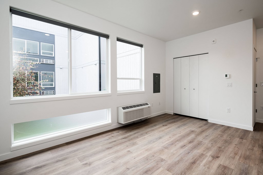 a living room with white walls and wood floors and a radiator and three windows