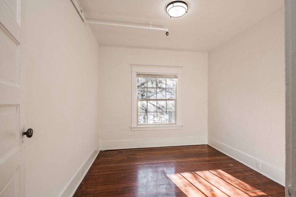 a living room with white walls and a window and wood floors