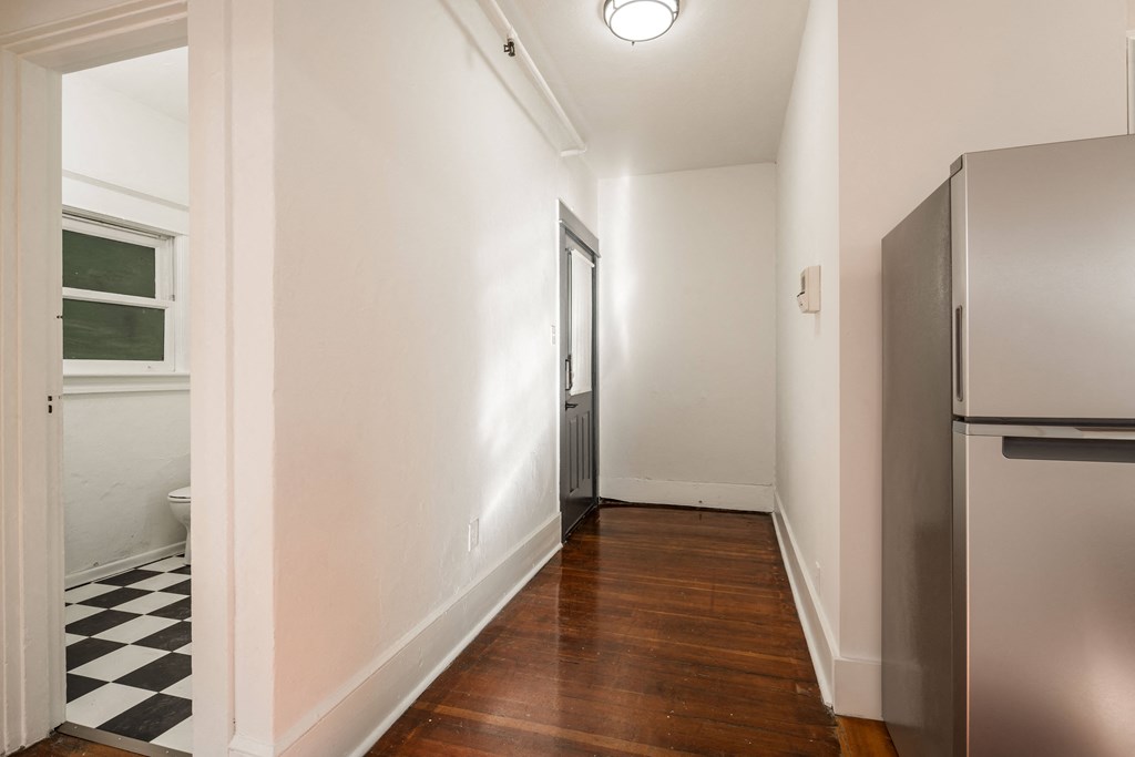 a renovated kitchen with white walls and wood floors and a stainless steel refrigerator