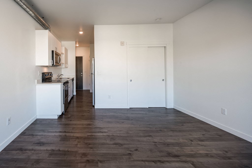 a kitchen and living room with white walls and wood flooring