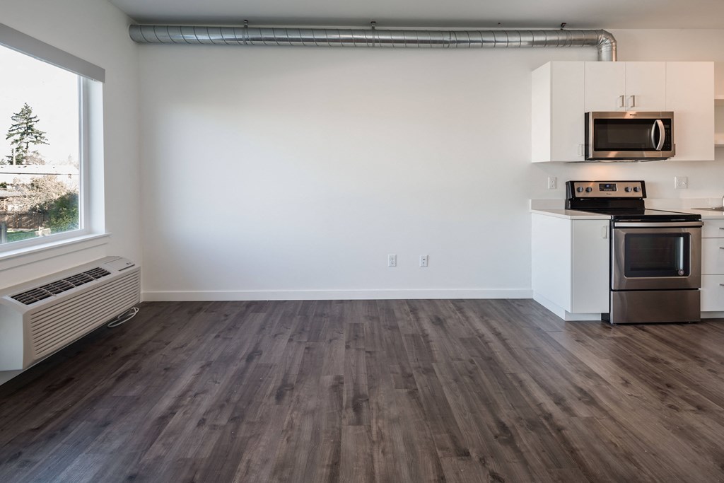 an empty living room with a kitchen and a window