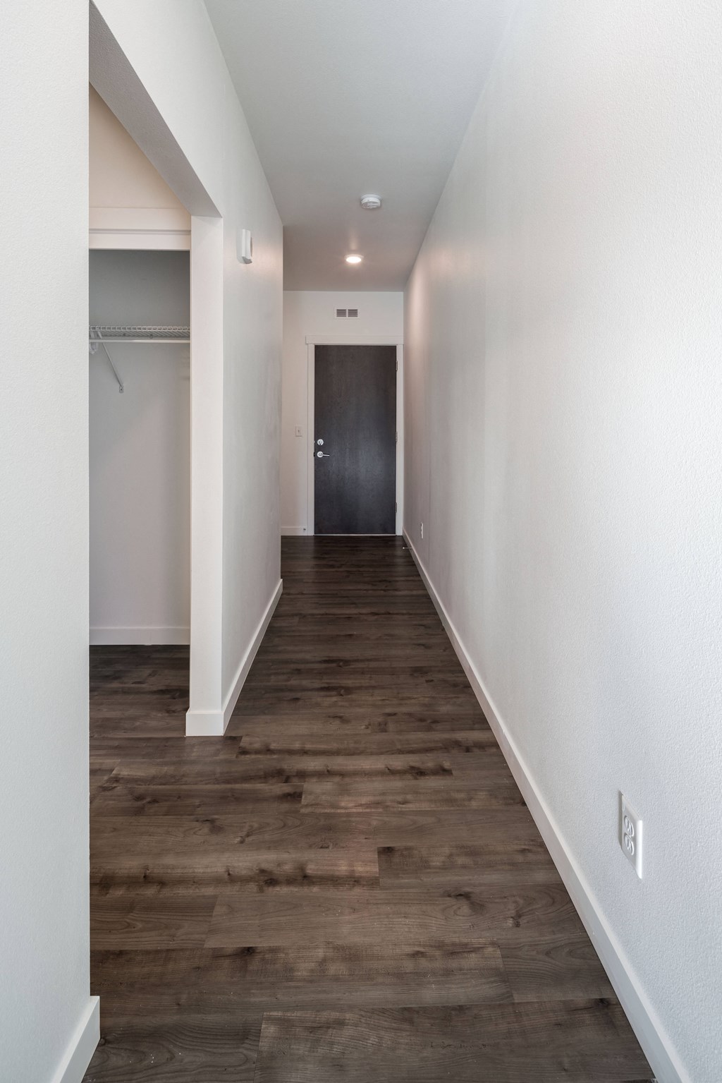 a hallway with white walls and a wooden floor and a black door