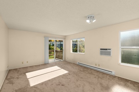 A spacious room with a carpeted floor and a sliding glass door leading to a balcony.