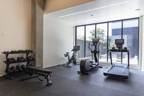 a gym with weights and cardio equipment in a room with large windows at Analog PDX Apartments, Portland, OR 97227