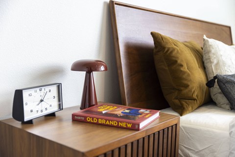 a clock and a book on a night stand next to a bed at Analog PDX Apartments, Oregon 97227