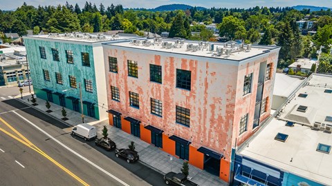 A multi-story building with a blue and pink facade is surrounded by trees and other buildings.