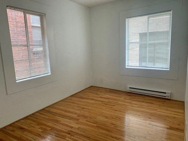 an empty room with wood floors and two windows