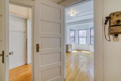 A white door with a brass handle is open to a room with wooden floors and a window.