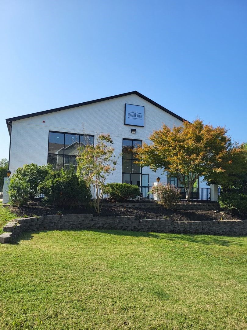 the front of a white building with a lawn and trees at Schaefer Ridge Apartments, Branson , MO