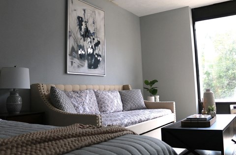 A living room with a grey couch and a large abstract painting on the wall.