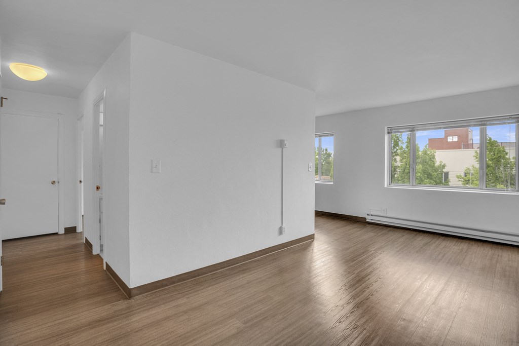 a living room with white walls and wood floors and a window