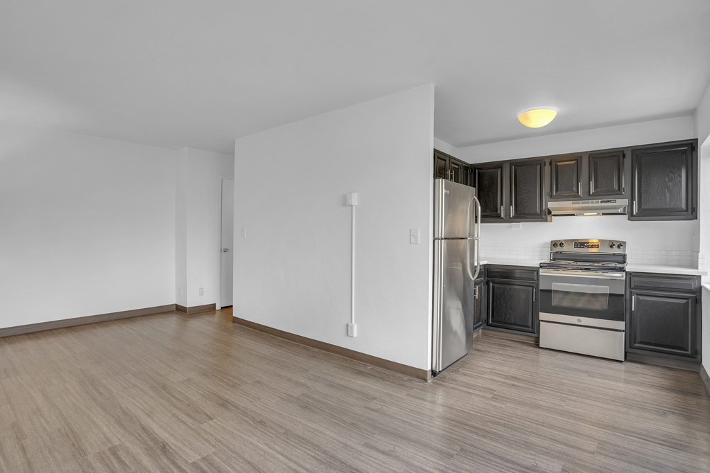 an empty kitchen with white walls and wood flooring and a stainless steel refrigerator