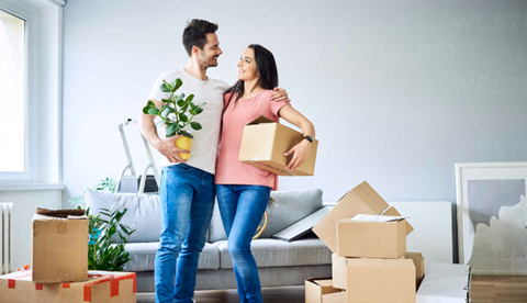 a man and a woman standing in a living room with boxes