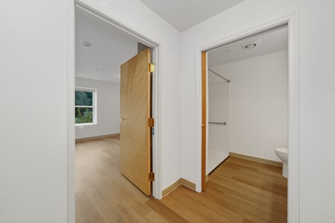 A room with a wooden floor and white walls with a door open to a bathroom.