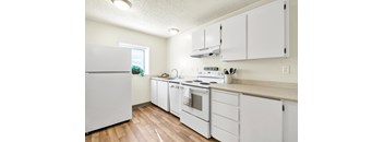 A white kitchen with wood floors and white appliances.