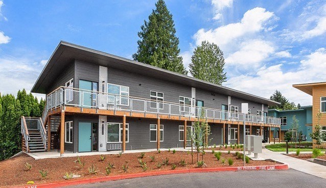 a gray apartment building with a balcony and trees in the background