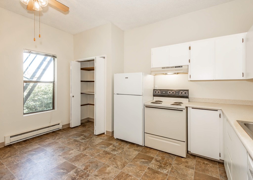 A kitchen with white appliances and brown tiled floors.