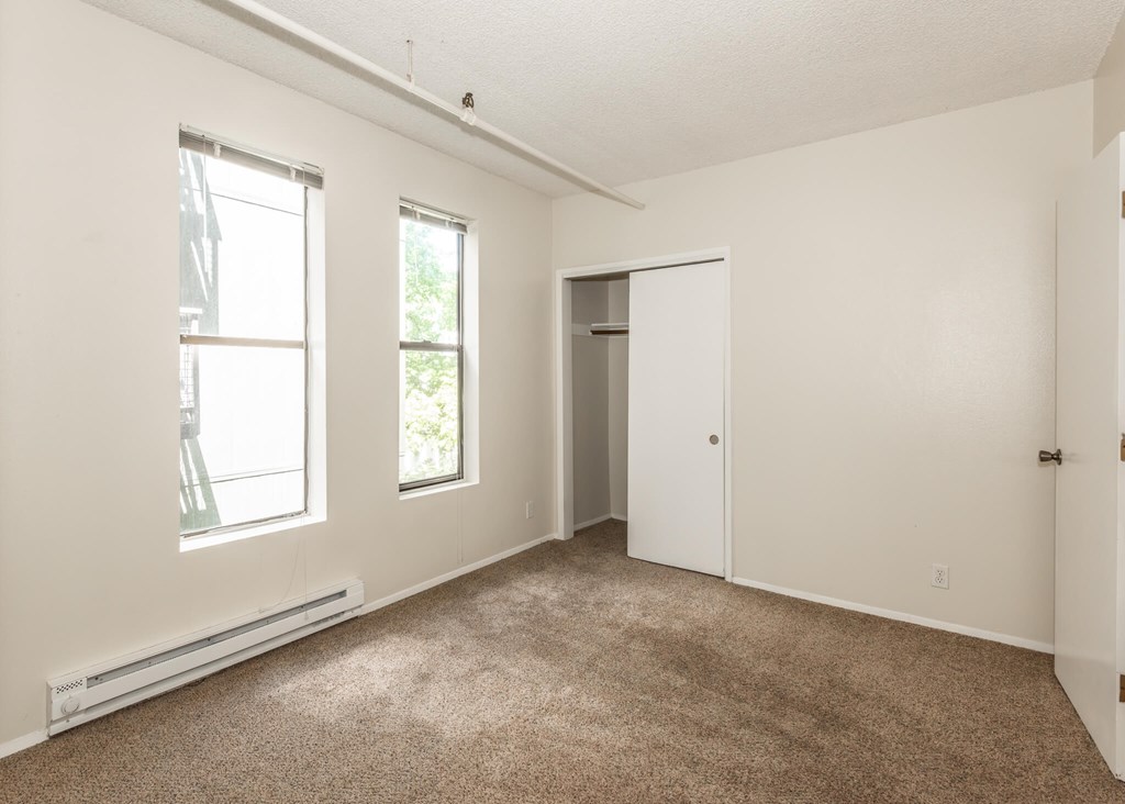 A room with a carpeted floor, two windows, and a door.