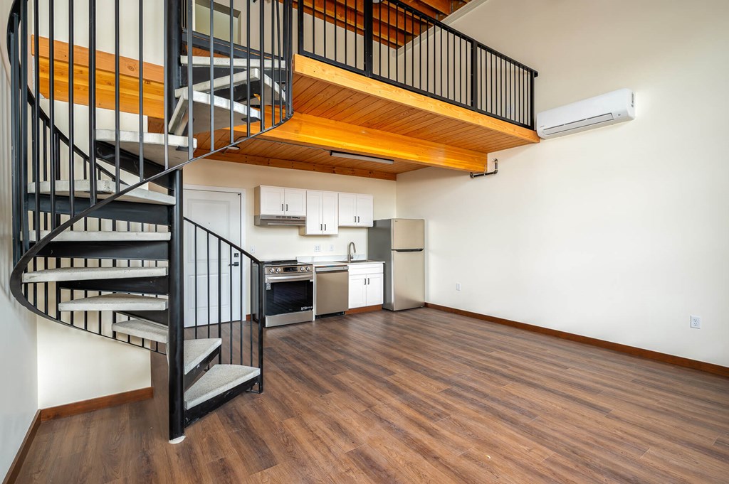 A spiral staircase with a wooden top leads to a kitchen area.