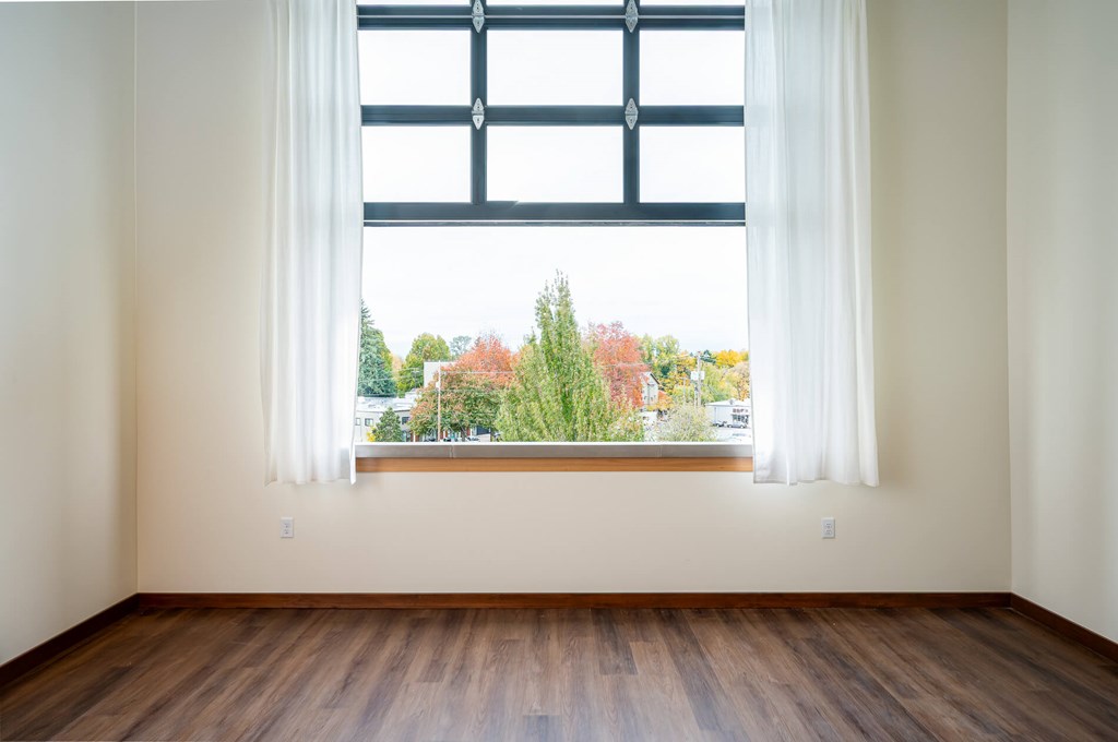 A room with a large window overlooking a tree-filled street.
