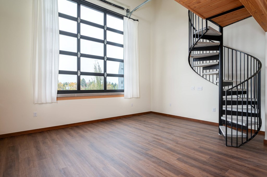 A spiral staircase in a room with wooden floors and a large window.