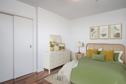 A bedroom with a bed, nightstand, and a plant on the nightstand.