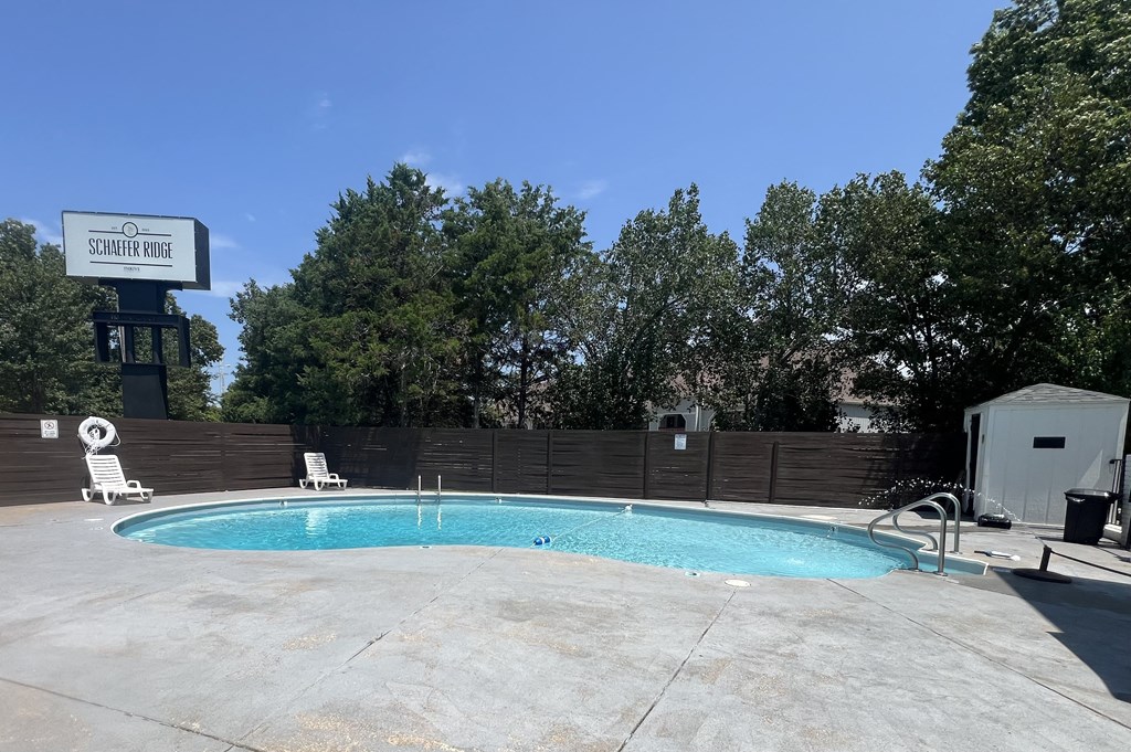 a swimming pool at a hotel with a fence and trees at Schaefer Ridge Apartments, Missouri