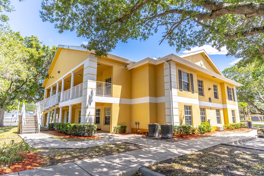 A yellow and white two-story house with a porch and a tree in front.