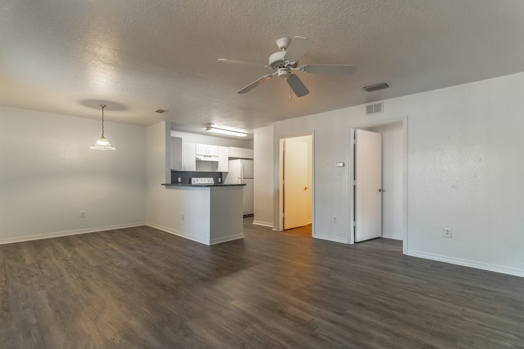 A room with a ceiling fan and a kitchenette in the background.