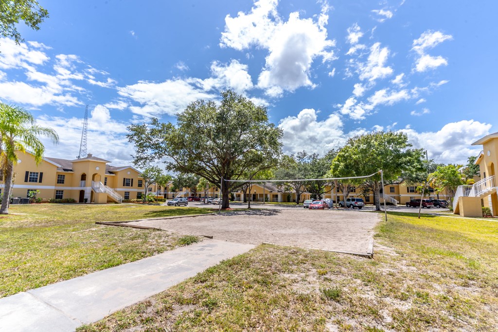 A playground with a volleyball net and a basketball hoop is surrounded by buildings and trees.
