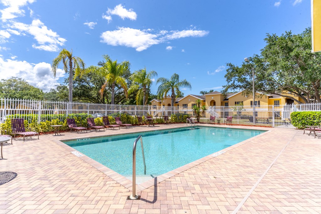 A pool surrounded by a white fence and palm trees.