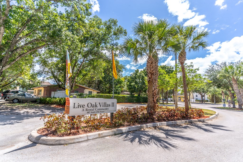 A sign for Live Oak Villas II, a rental community, is displayed in front of a landscaped area with palm trees.