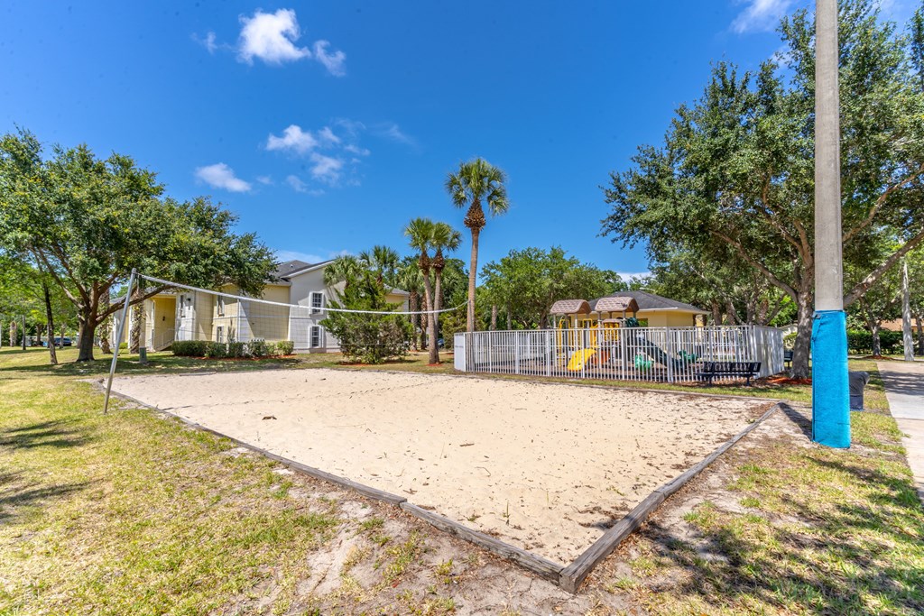 A sandy playground area with a blue pole and a fence in the background.