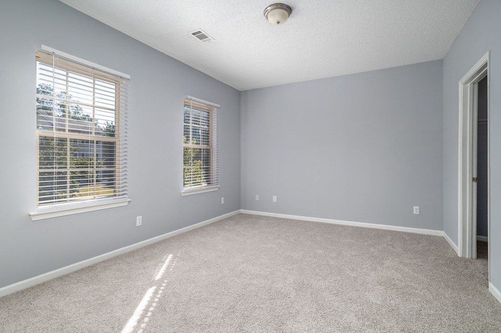 a bedroom with three windows and a carpeted floor