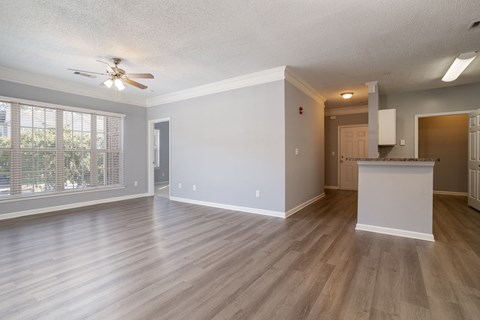 an empty living room with a kitchen in the background