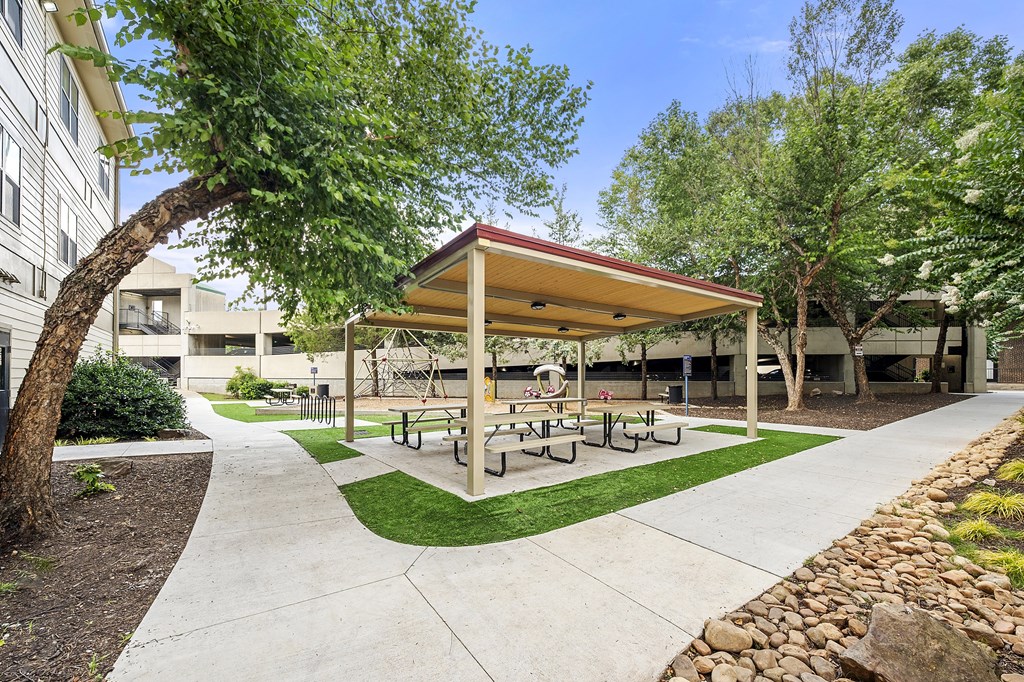 A covered picnic area with benches is surrounded by trees.