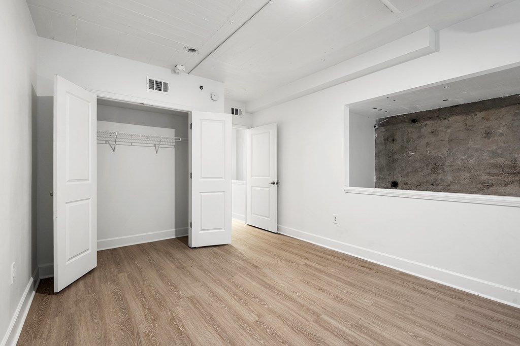 A room with white walls and wooden flooring, with a large open doorway leading to another room.