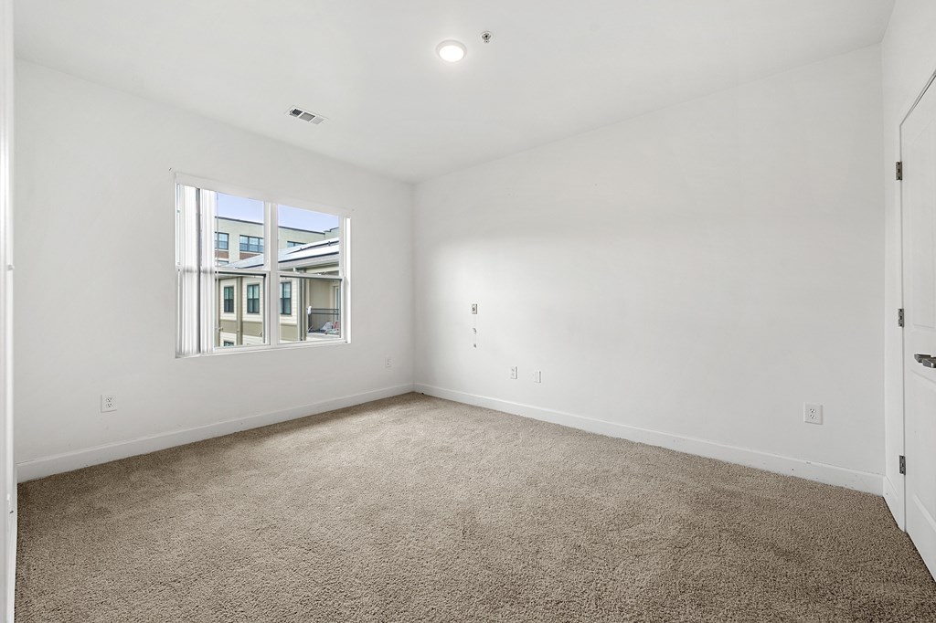 A large empty room with a carpeted floor and a window.