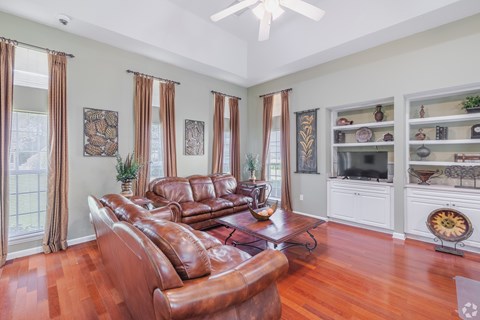 A living room with a brown leather couch and a fan on the ceiling.