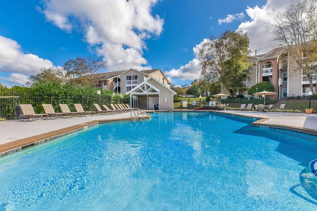 a swimming pool with lounge chairs and umbrellas in front of a house
