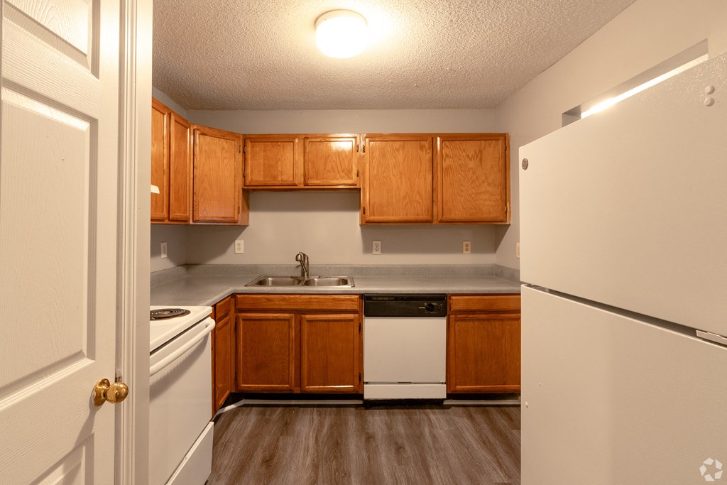 an empty kitchen with white appliances and wooden cabinets at Avon Crossings, Durham, NC 27713