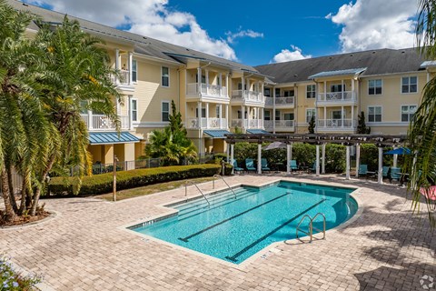 A large swimming pool is surrounded by a brick patio and palm trees.