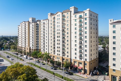 A row of apartment buildings with cars parked in front.