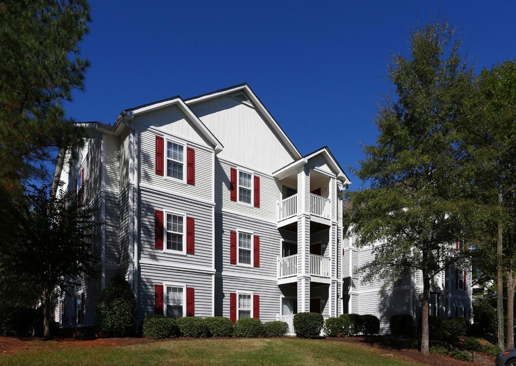 a gray apartment building with red shutters and a blue sky in the background at Avon Crossings, Durham, NC