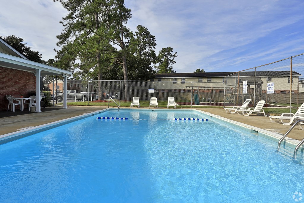 A large blue swimming pool with white lounge chairs around it. A large blue swimming pool with white lounge chairs around it.at Brandywine Townhomes, Goose Creek, SC 29445