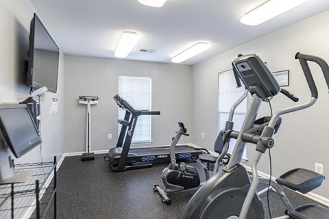 A spacious gym with a treadmill, elliptical trainer, and a television at English Oaks Apartments, Virginia, 22406