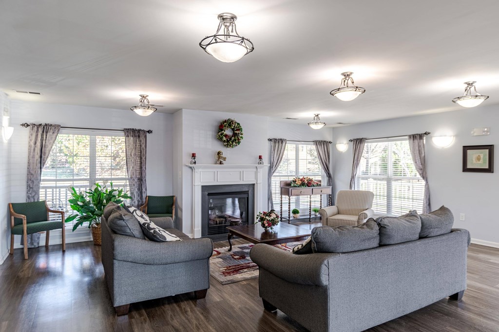 A living room with a grey couch, a green chair, and a fireplace at English Oaks Apartments, Virginia