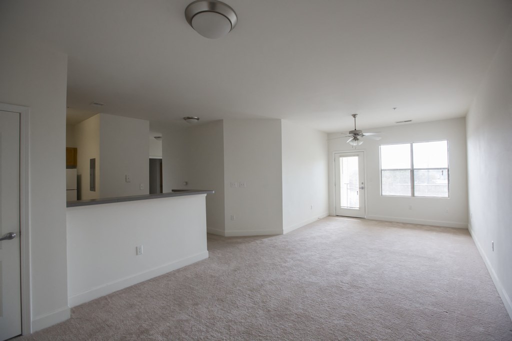 an empty living room with a kitchen in the background