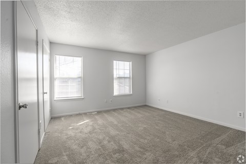 the living room of an apartment with carpet and two windows