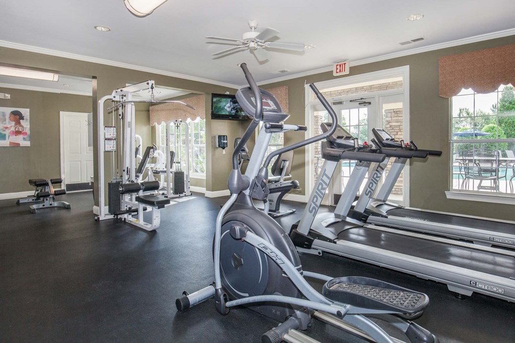 a gym with a row of workout equipment and windows at Carrington Place at Wildewood, Columbia, SC  